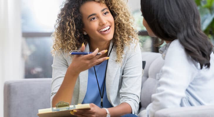 5 Client Touchpoints to Wow Your Real Estate Positive young female therapist gestures as she talks with a female client. The therapist smiles warmly as she talks with the young woman.